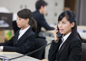 オフィスデスクでビジネスフォン受話器を持ち通話（会話）している女性イメージ